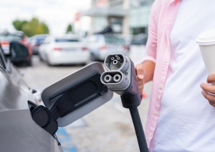 Mann mit CCS-Stecker auf einem Parkplatz beim Laden seines E-Autos